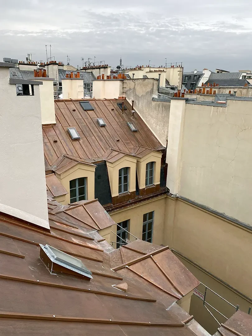 Vue aérienne d'une toiture parisienne avec couverture en zinc patiné, lucarnes à frontons, chéneaux et descentes pluviales