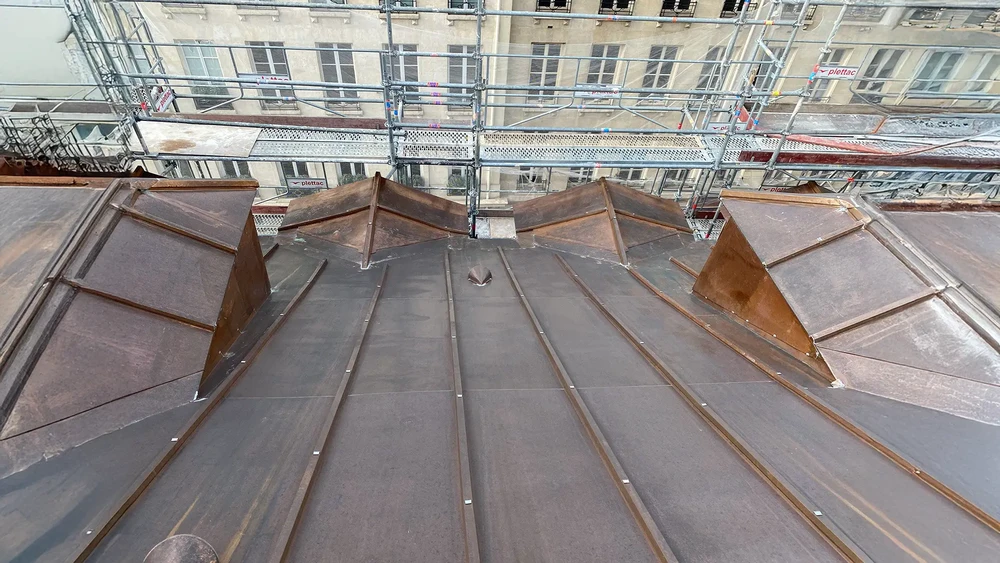 Chantier de rénovation de toiture en cours avec échafaudages métalliques sécurisés autour d'un bâtiment historique