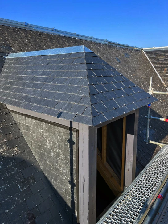 Ouvrier couvreur en vêtements de sécurité installant une nouvelle toiture sur maison résidentielle