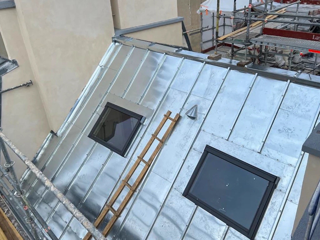 Toiture m&eacute;tallique moderne avec chemin&eacute;e en acier gris sous ciel nuageux au coucher du soleil, environnement r&eacute;sidentiel bois&eacute;