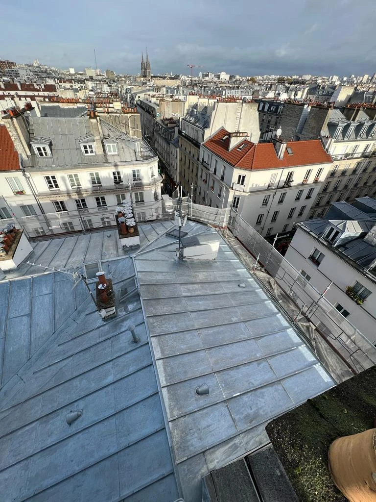 Vue aérienne d'une toiture parisienne avec couverture en zinc patiné, lucarnes à frontons, chéneaux et descentes pluviales